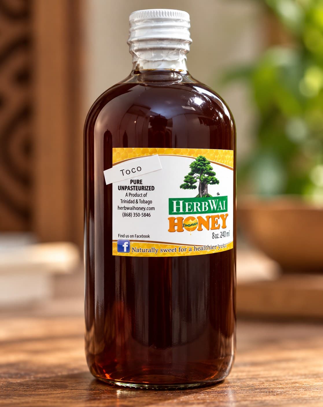 Round bottle of dark amber HerbWai Toco honey, labelled Toco, Pure Unpasteurized, on a wooden table